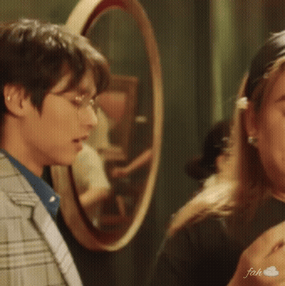 A Man In A Suit And Glasses Is Standing Next To A Woman In Front Of A Mirror . GIF
