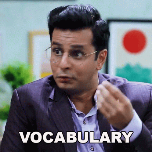 A Man In A Suit And Glasses Says Vocabulary With His Hand GIF