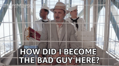 A Man In A Suit And Hat Is In A Ferris Wheel Behind Bars And Says How Did I Become The Bad Guy Here GIF