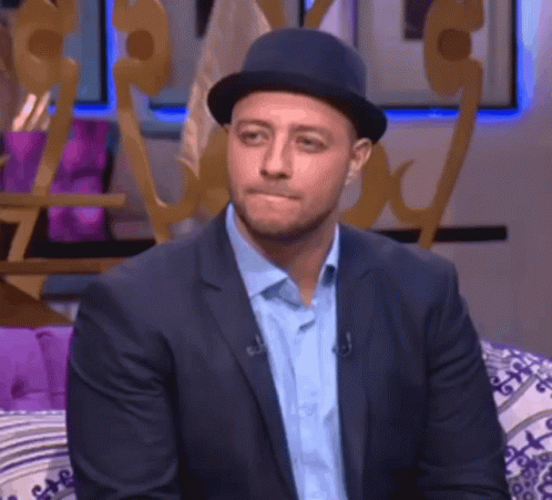 A Man In A Suit And Hat Is Sitting On A Couch With His Eyes Closed GIF
