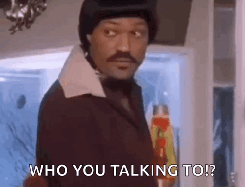 A Man In A Suit And Hat Is Standing In Front Of A Door And Talking To Someone . GIF