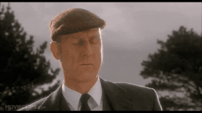 A Man In A Suit And Hat Is Standing In Front Of Some Trees . GIF
