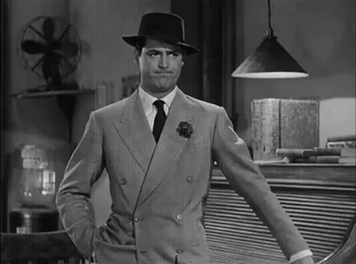 A Man In A Suit And Hat Is Standing With His Hands In His Pockets . GIF