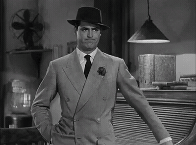 A Man In A Suit And Hat Is Standing With His Hands In His Pockets In A Black And White Photo . GIF
