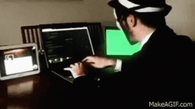 A Man In A Suit And Hat Is Typing On A Laptop Computer . GIF