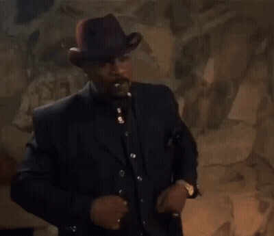 A Man In A Suit And Hat Smoking A Cigarette GIF