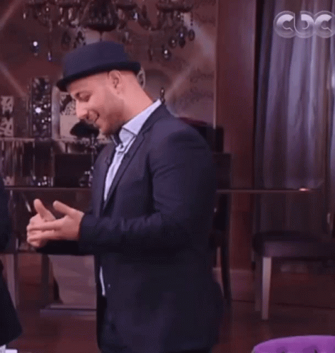 A Man In A Suit And Hat Talks To A Woman In Front Of A Cdg Sign GIF