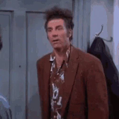 A Man In A Suit And Hawaiian Shirt Is Standing In Front Of A Locker . GIF