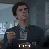 A Man In A Suit And Plaid Shirt Is Holding A Cell Phone And A Pen . GIF