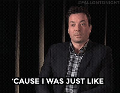 A Man In A Suit And Plaid Shirt Is Waving His Hand In Front Of A Black Curtain With #Fallontonight Written On It GIF