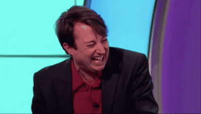 A Man In A Suit And Red Shirt Is Laughing On A Stage GIF