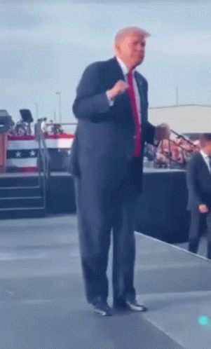A Man In A Suit And Red Tie Is Standing On A Stage GIF