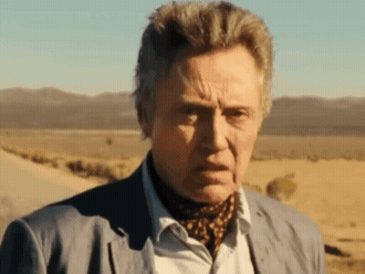 A Man In A Suit And Scarf Is Standing In A Desert GIF