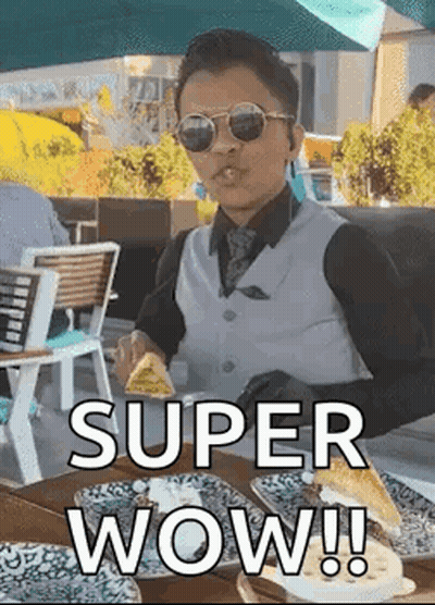 A Man In A Suit And Sunglasses Is Sitting At A Table Eating A Sandwich . GIF