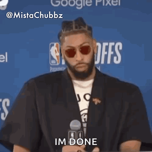 A Man In A Suit And Sunglasses Is Sitting In Front Of A Microphone . GIF