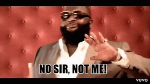 A Man In A Suit And Sunglasses Is Sitting In Front Of A Red Couch . GIF