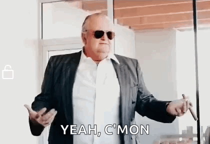 A Man In A Suit And Sunglasses Is Smoking A Cigar And Saying `` Yeah , C 'Mon '' . GIF