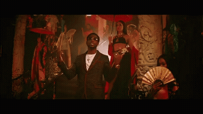 A Man In A Suit And Sunglasses Is Standing Next To A Woman In A Bikini And Holding A Fan . GIF