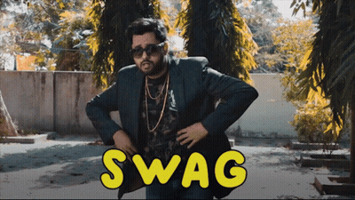 A Man In A Suit And Sunglasses Stands In Front Of A Sign That Says Swag On It GIF