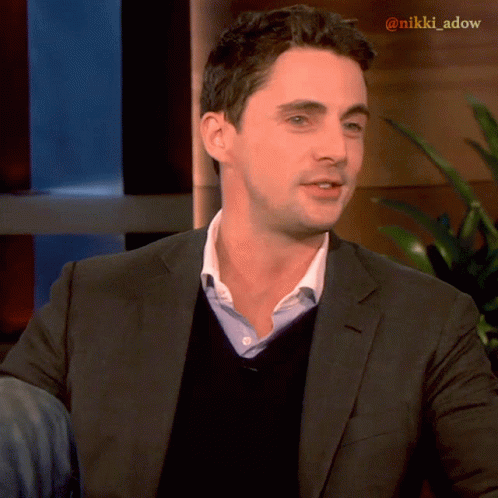 A Man In A Suit And Sweater With The Name Nikki Adow On The Bottom Right GIF
