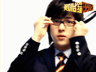 A Man In A Suit And Tie Adjusts His Glasses In Front Of A Sign That Says 2012 GIF