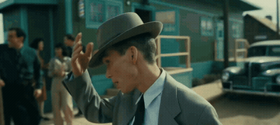 A Man In A Suit And Tie Adjusts His Hat In Front Of A Barber Shop GIF