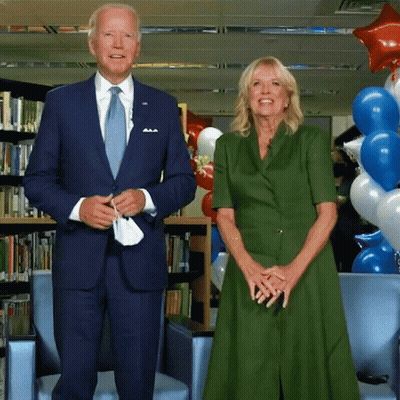A Man In A Suit And Tie And A Woman In A Green Dress Stand Next To Each Other GIF