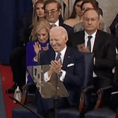 A Man In A Suit And Tie Applauds While Sitting In A Crowd GIF