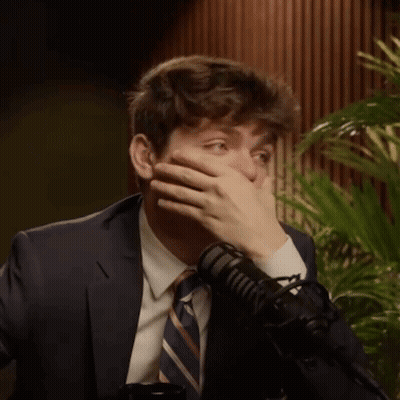 A Man In A Suit And Tie Covers His Mouth With His Hand GIF