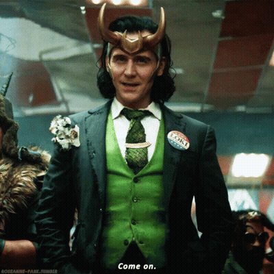 A Man In A Suit And Tie Has A Loki Bumper Sticker On His Vest GIF