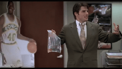 A Man In A Suit And Tie Holds A Bag In Front Of A Sonics Basketball Player GIF