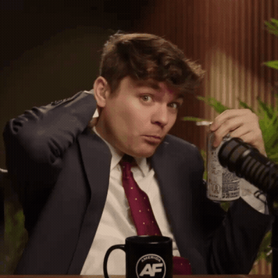 A Man In A Suit And Tie Holds A Can Of Soda In Front Of A Microphone And A Mug That Says American Af GIF
