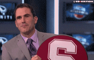 A Man In A Suit And Tie Holds A Circle With A Letter C On It GIF