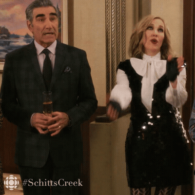 A Man In A Suit And Tie Holds A Glass Of Champagne Next To A Woman In A Black And White Sequined Dress GIF