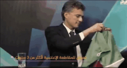 A Man In A Suit And Tie Holds A Green Shirt In His Hand GIF