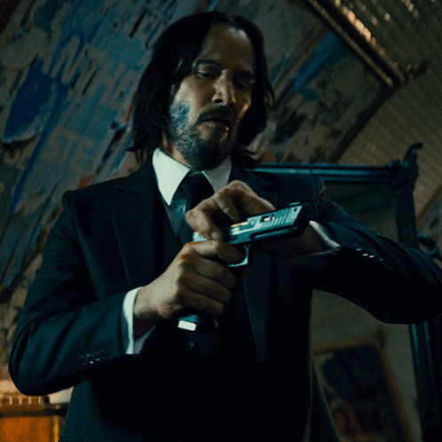 A Man In A Suit And Tie Holds A Gun In His Hand GIF