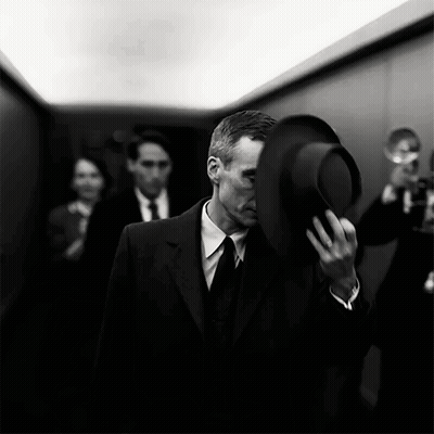 A Man In A Suit And Tie Holds A Hat Over His Face GIF