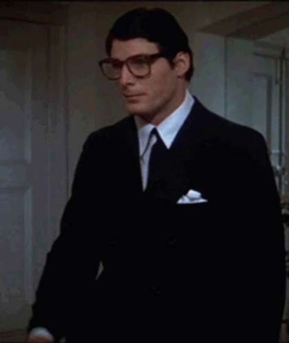 A Man In A Suit And Tie Holds A Pair Of Glasses In His Hand GIF