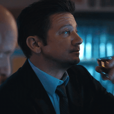 A Man In A Suit And Tie Holds A Small Glass GIF
