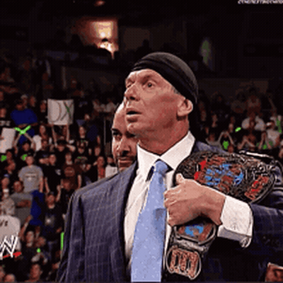 A Man In A Suit And Tie Holds A Wrestling Belt Over His Shoulder GIF
