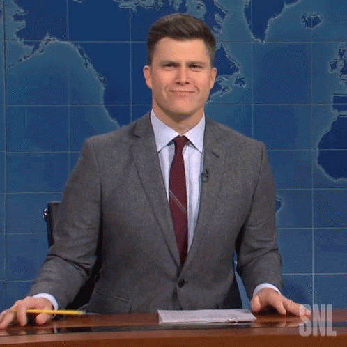 A Man In A Suit And Tie Holds A Yellow Pencil In Front Of A Snl Sign GIF