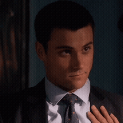 A Man In A Suit And Tie Holds His Hand To His Chest GIF