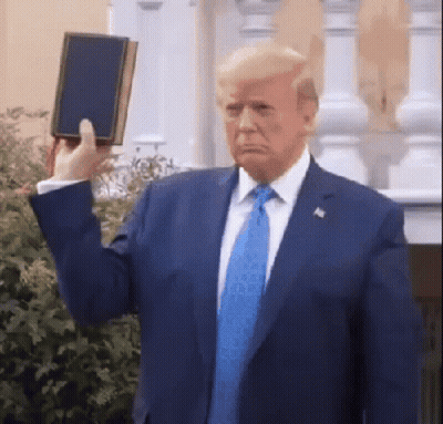A Man In A Suit And Tie Holds Up A Bible GIF