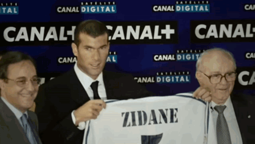 A Man In A Suit And Tie Holds Up A Zidane Shirt GIF