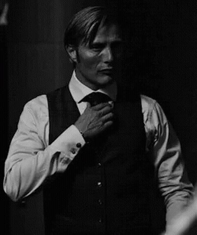 A Man In A Suit And Tie Is Adjusting His Jacket . GIF