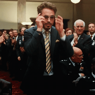 A Man In A Suit And Tie Is Adjusting His Sunglasses In Front Of A Crowd GIF