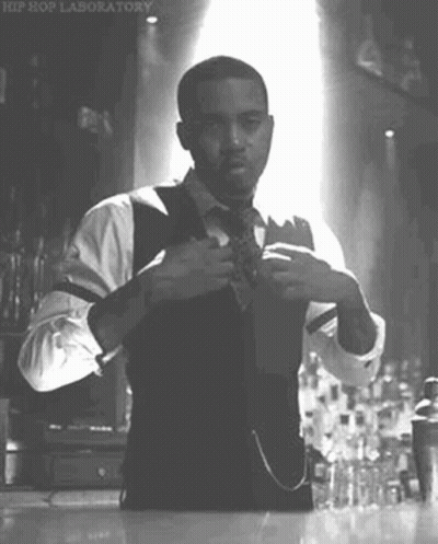 A Man In A Suit And Tie Is Adjusting His Tie In A Black And White Photo . GIF