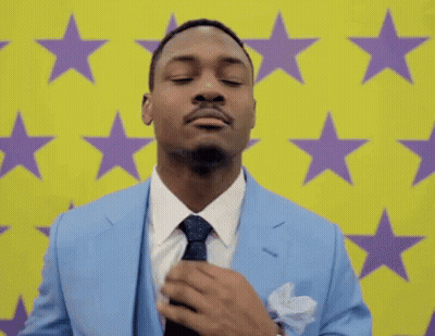 A Man In A Suit And Tie Is Adjusting His Tie In Front Of A Yellow Background With Purple Stars . GIF