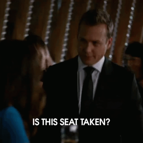 A Man In A Suit And Tie Is Asking Is This Seat Taken GIF