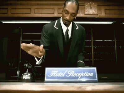 A Man In A Suit And Tie Is Behind A Hotel Reception Desk GIF
